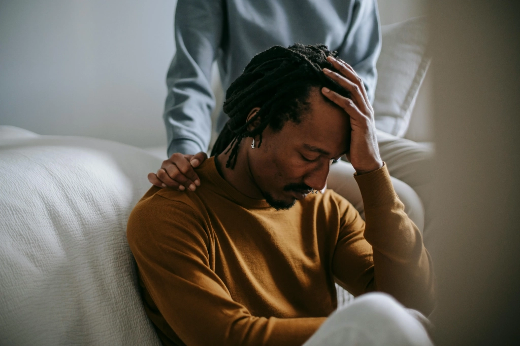 grief coloured man sitting on couch being comforted