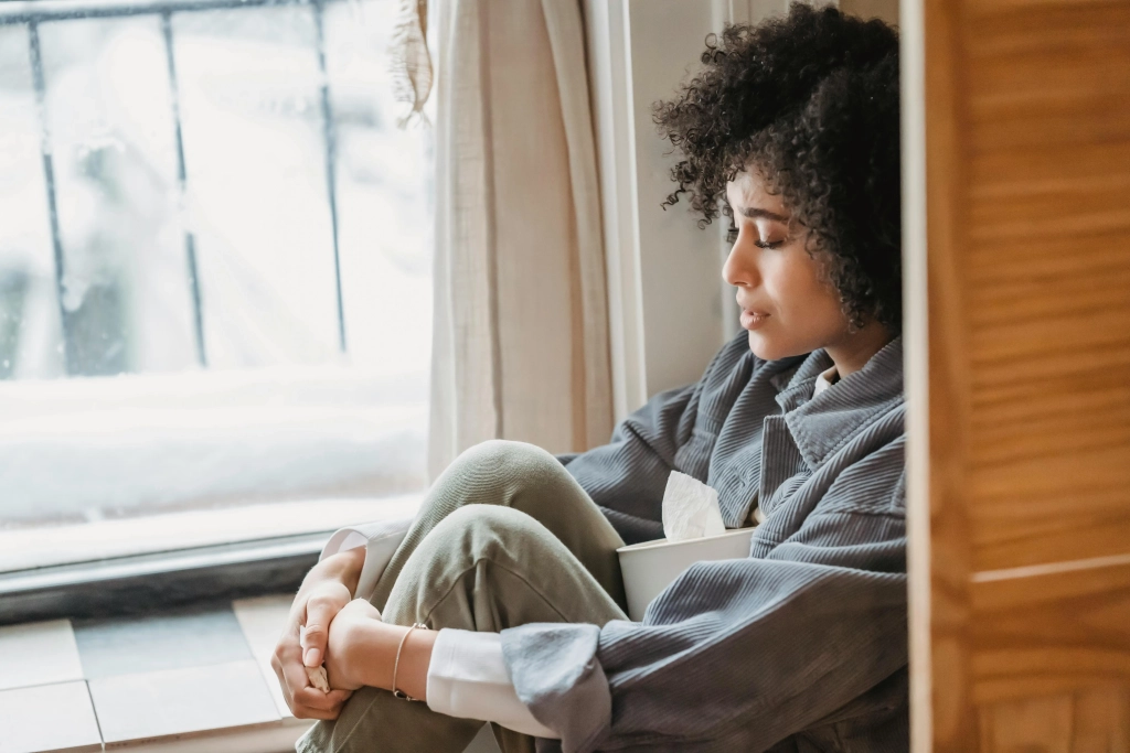 African American woman seeking solace against a wall with a tissue box in Cochrane & Calgary, embodying the need for anxiety therapy.